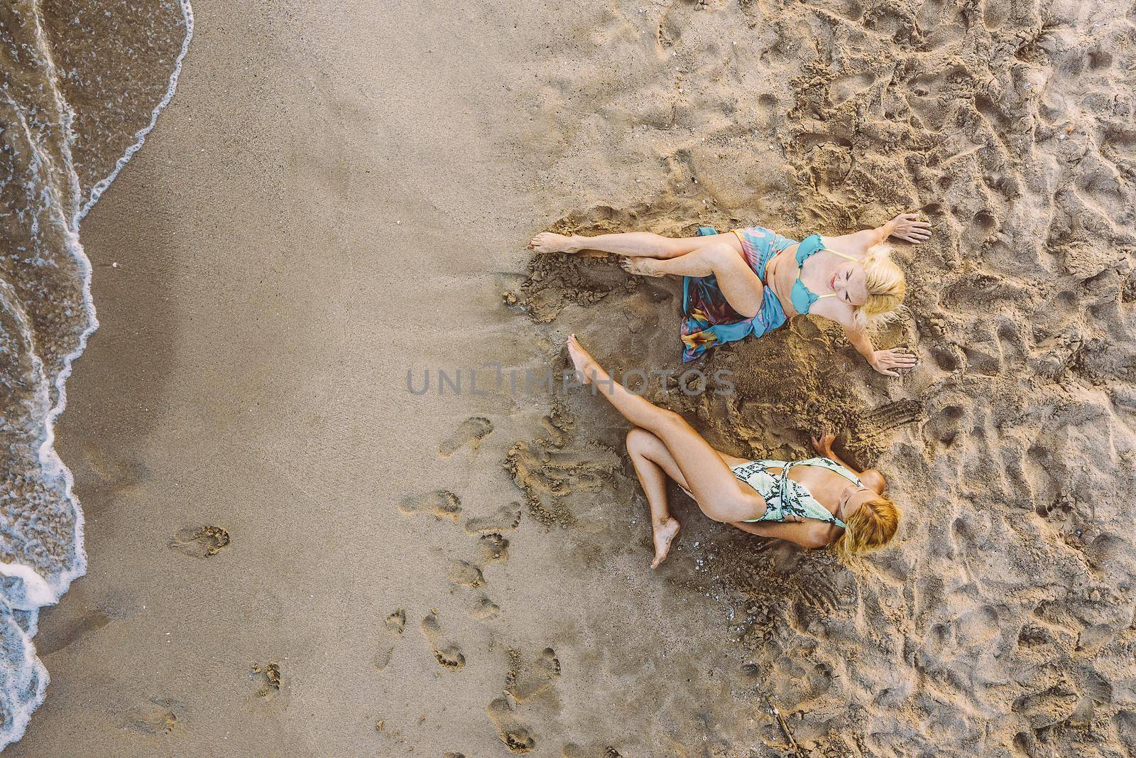 top view of two blond girls lying on the sand by the sea, concept of friendship and relaxation in the summer