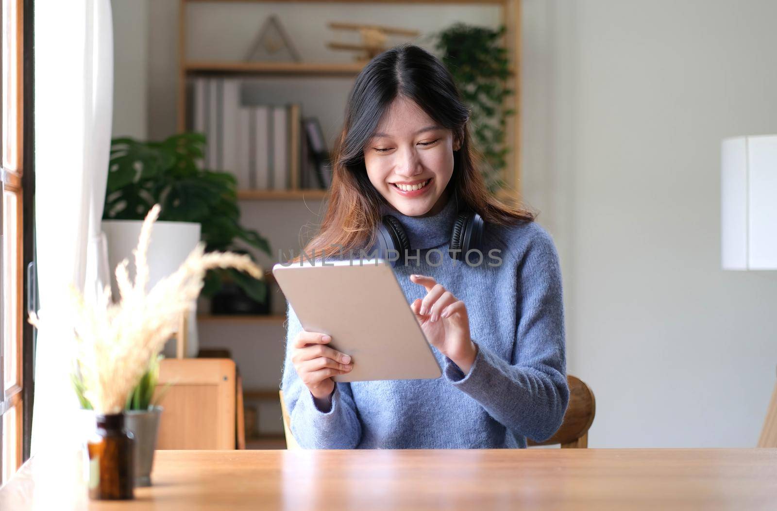Portrait of smiling happy beautiful asian woman relaxing using technology of tablet while sitting on table.Young creative girl working and typing on keyboard at home.work at home concept.
