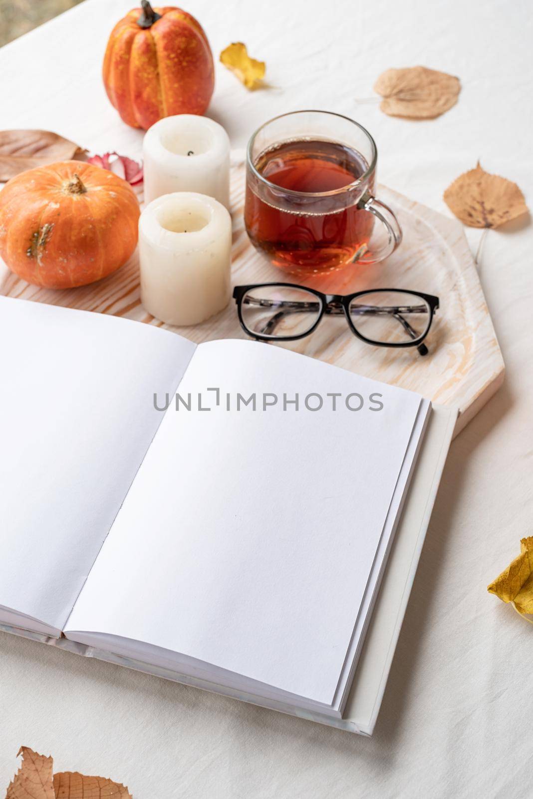 white blank book with autumn leaves, glasses and candles on white table , mockup design by Desperada
