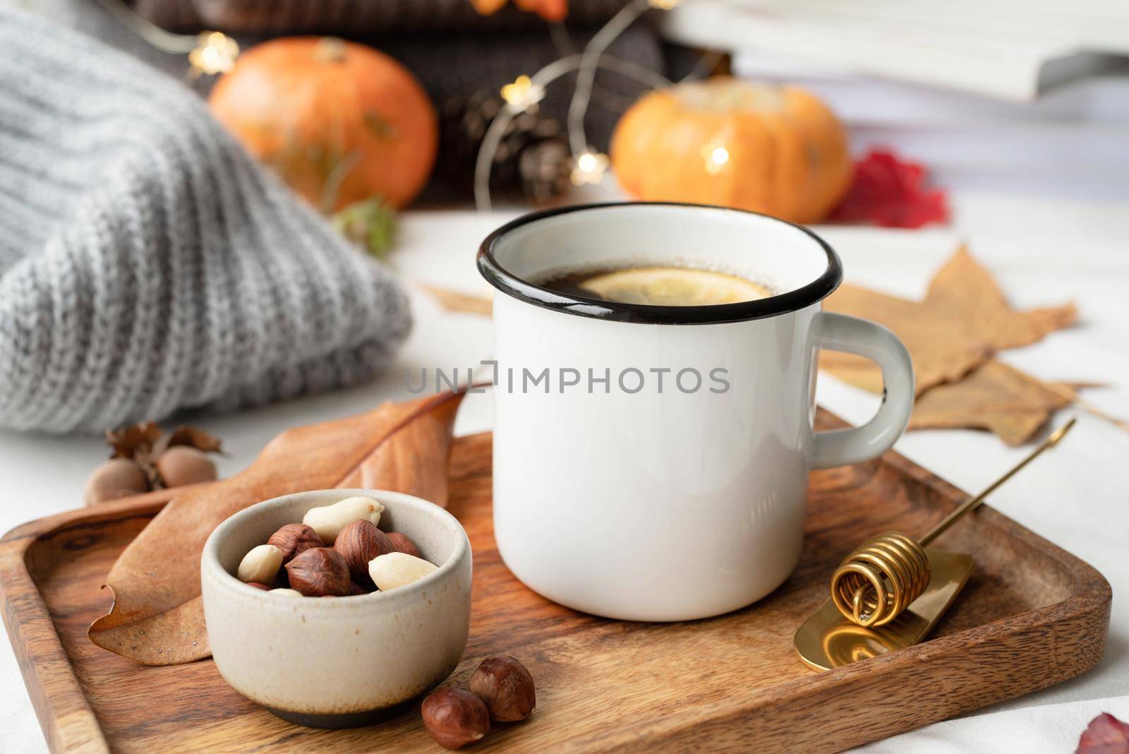 Hello fall. Cozy warm image. Cozy autumn composition, sweater weather. Hot tea with lemon and nuts on wooden tray surrounded with autumn leaves and sweaters, mug mockup design