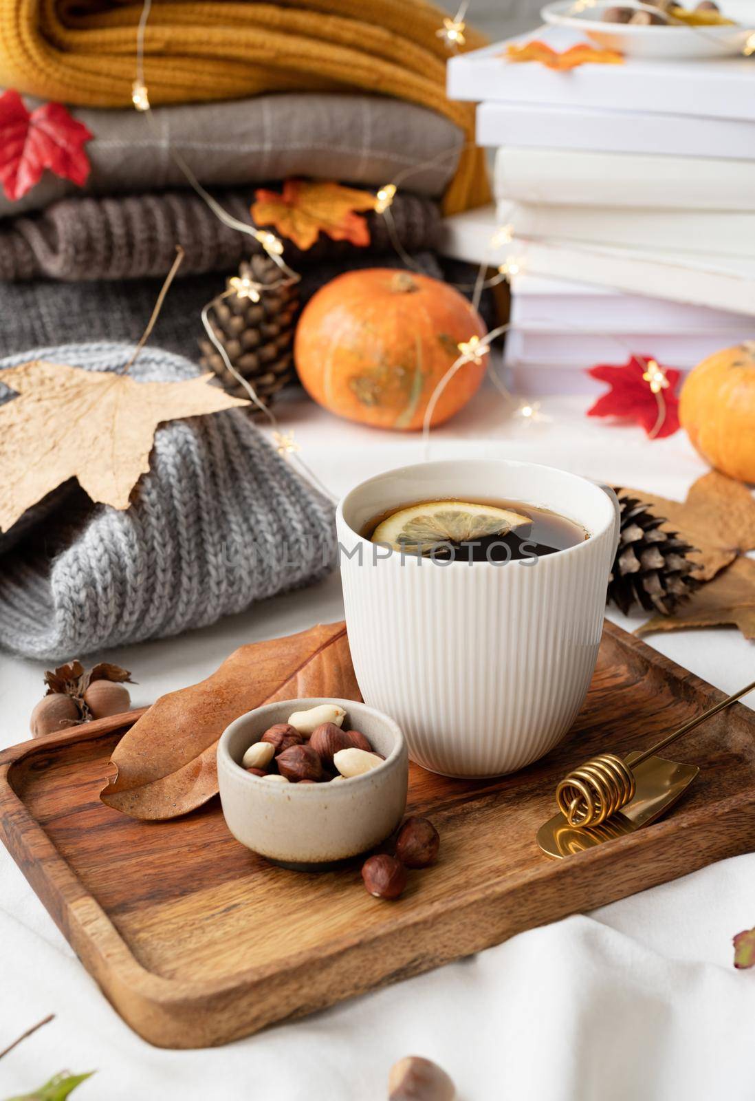 Hello fall. Cozy warm image. Cozy autumn composition, sweater weather. Hot tea with lemon and nuts on wooden tray surrounded with autumn leaves and sweaters