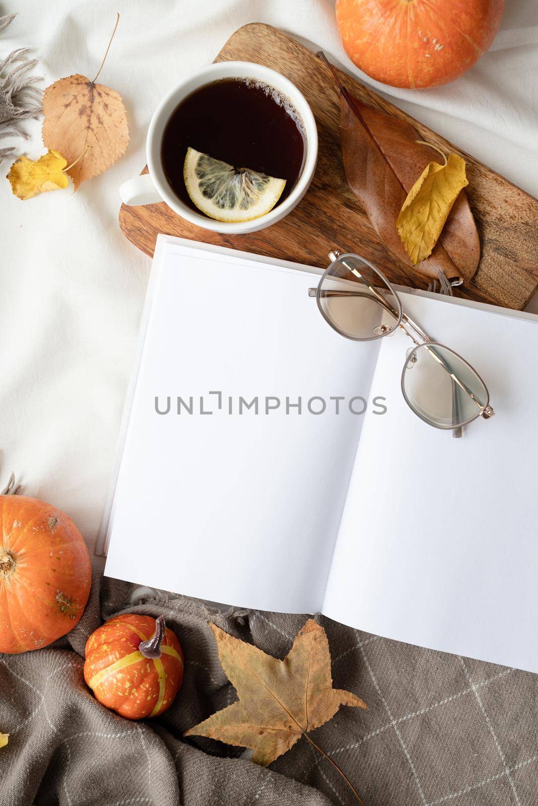 white blank book with autumn leaves and cup of hot tea on table , book mockup design by Desperada