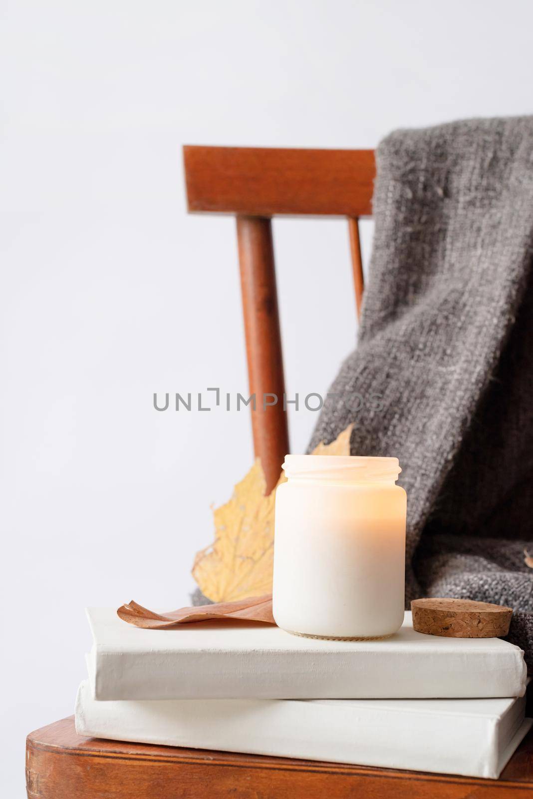 Hello fall. Cozy warm image. Candle mockup design. Cozy interior with old vintage chair, warm plaid, books and autumn leaves. Burning candle mockup design