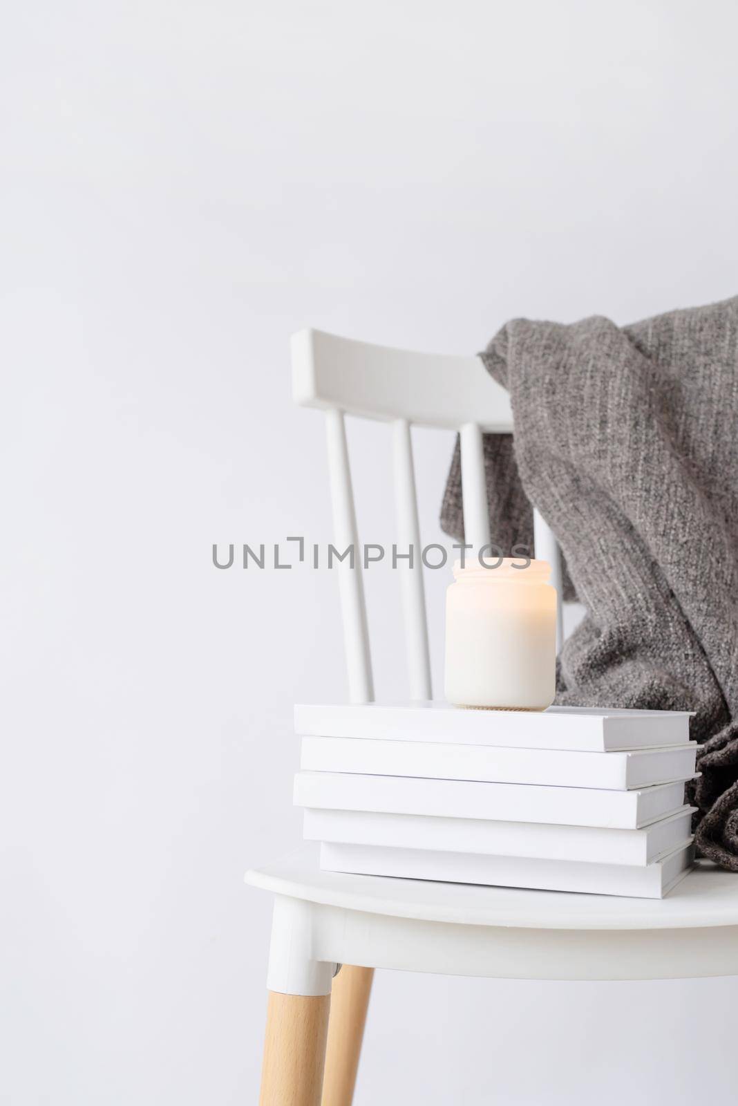 Hello fall. Cozy warm image. Candle mockup design. Cozy interior with white chair, warm plaid, books and autumn leaves. Burning candle mockup design