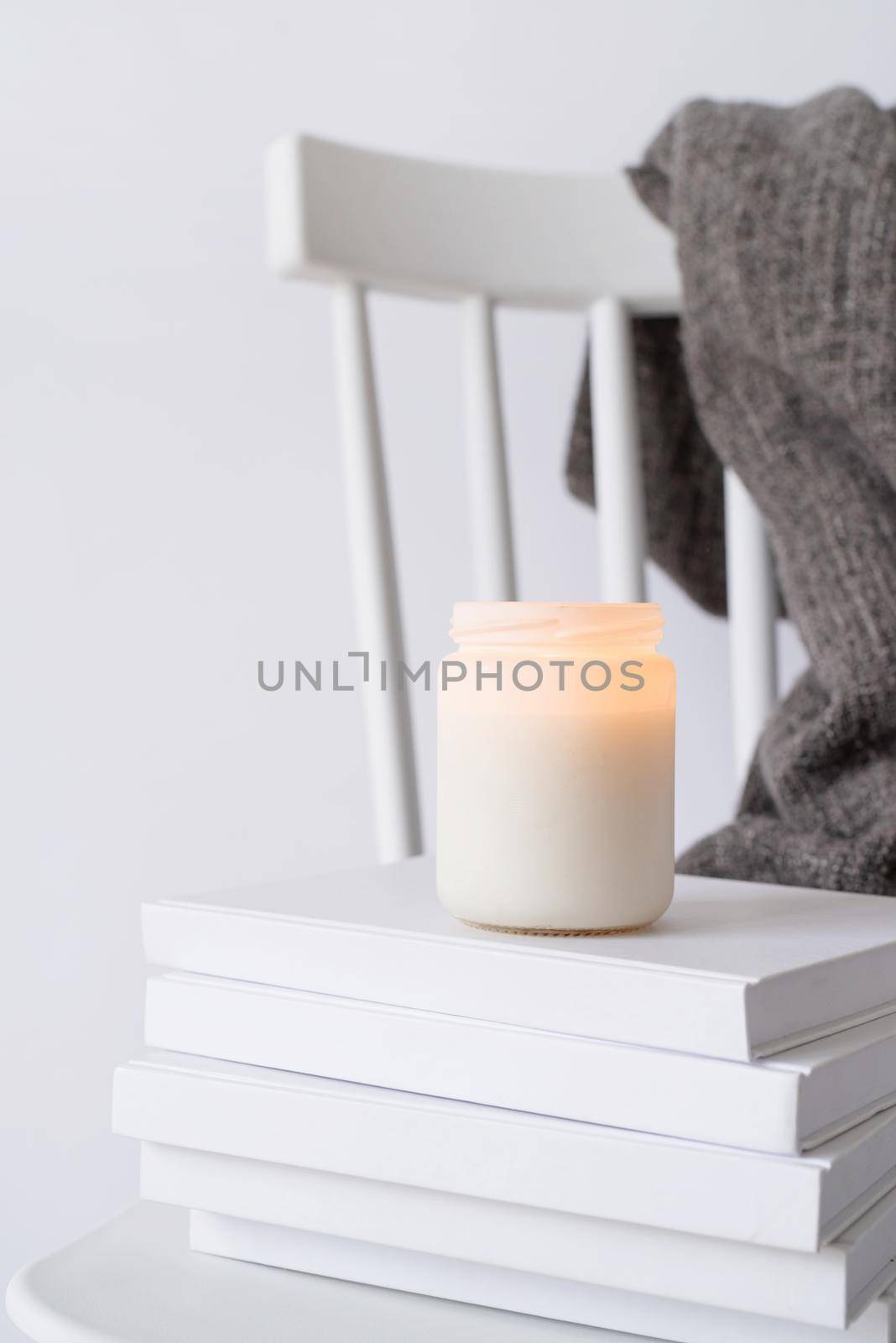 Candle mockup design. Cozy interior with white chair, warm plaid, books and autumn leaves by Desperada