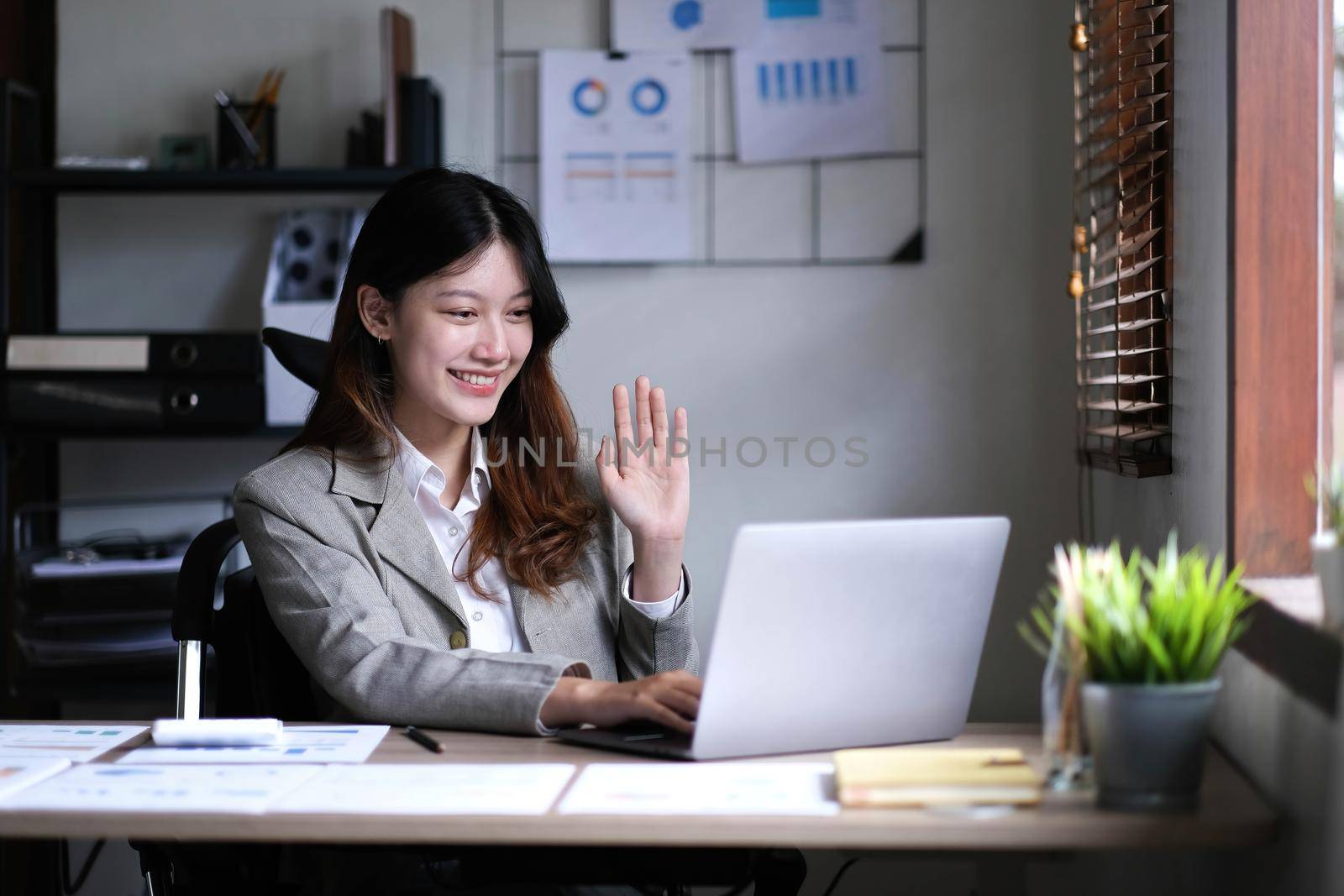Beautiful Asian businesswoman is on video call with customer on laptop in office and has a negotiating gesture. smiling and happy face. by wichayada