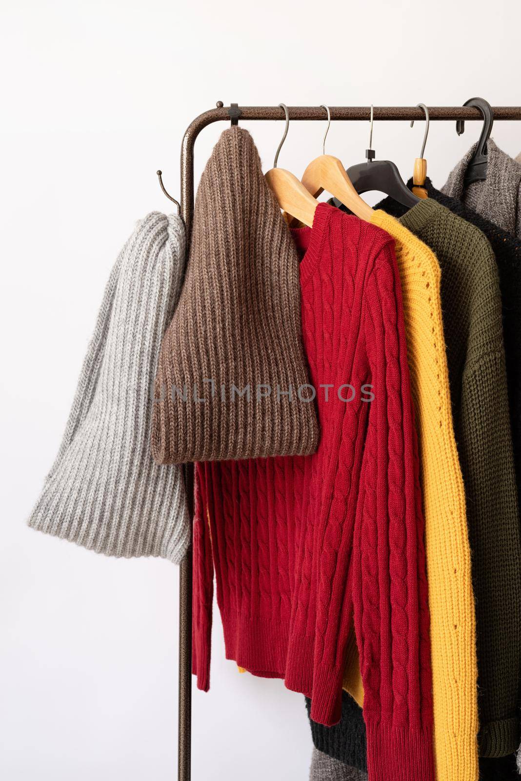 Row of different colorful Knitted sweaters hang on hangers, white background by Desperada
