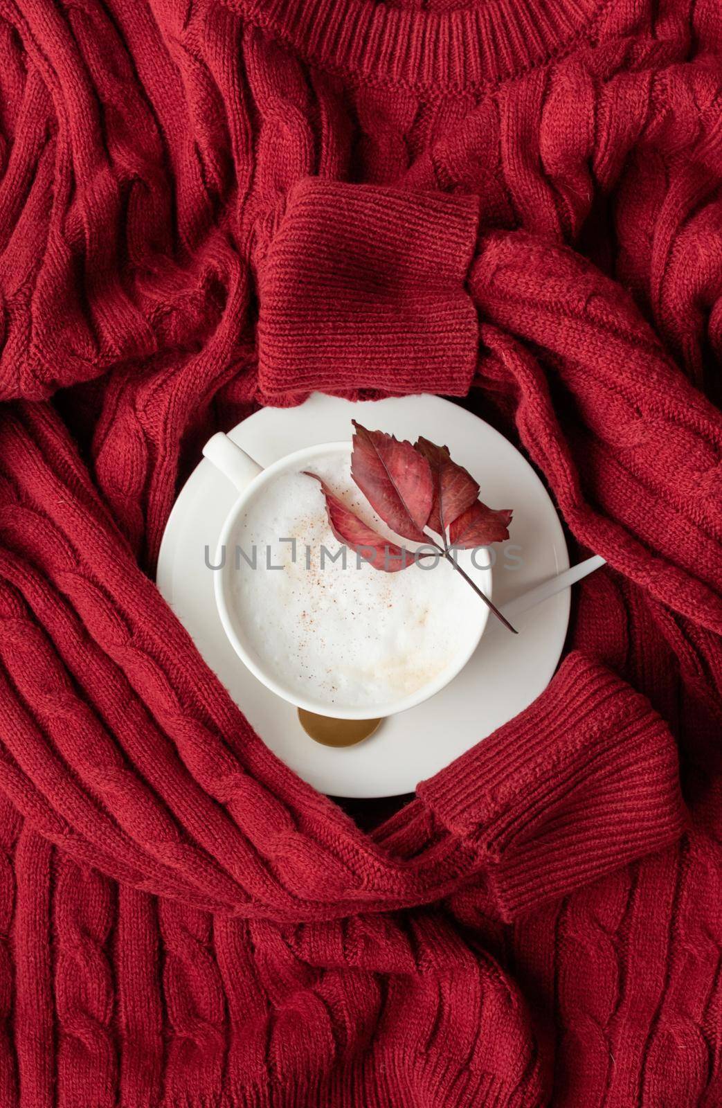 cup of cappuccino coffee on red sweater top view flat lay by Desperada