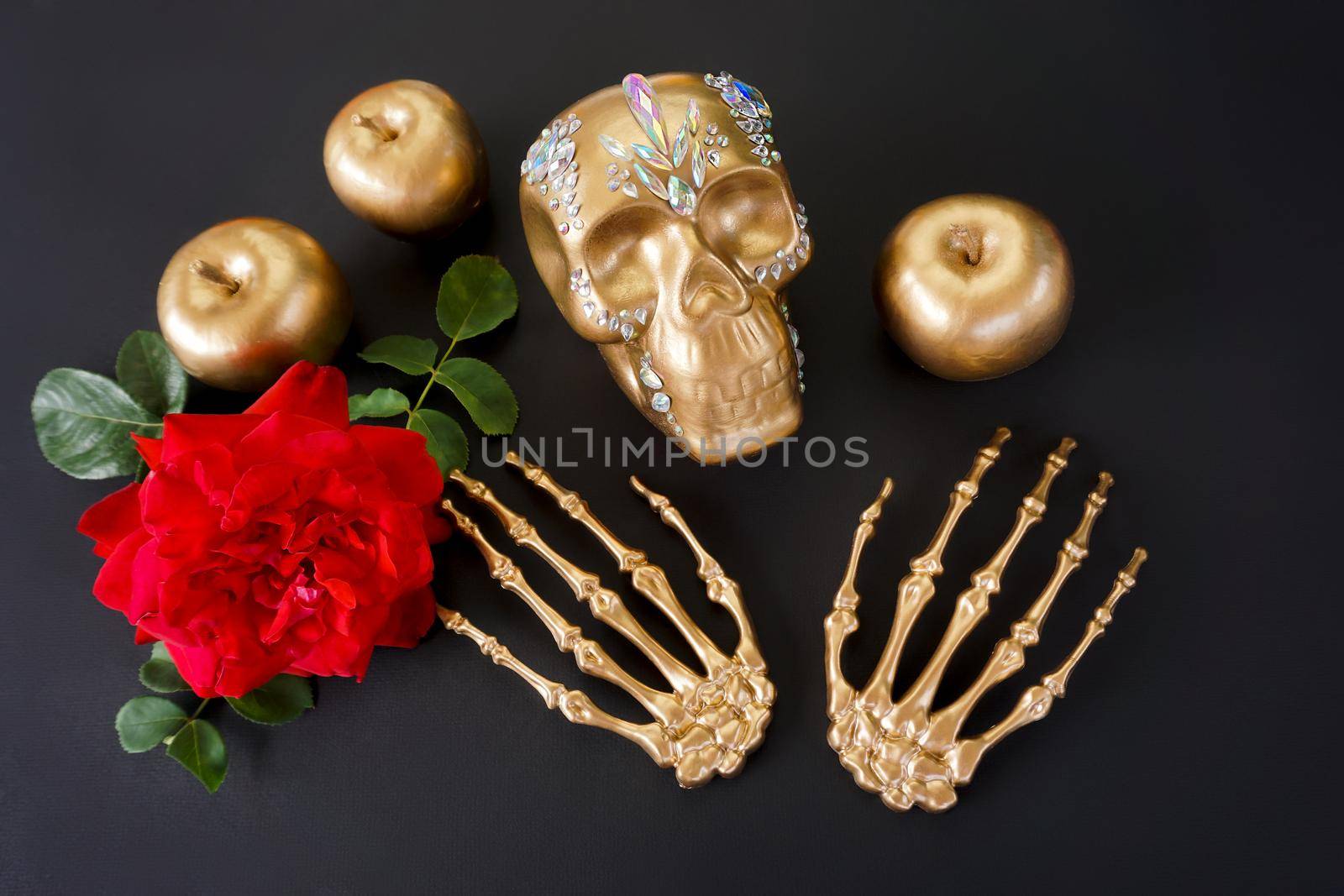 The golden skull is decorated with rhinestones, the paws of a skeleton, a red rose and treats made of apples lie next to it