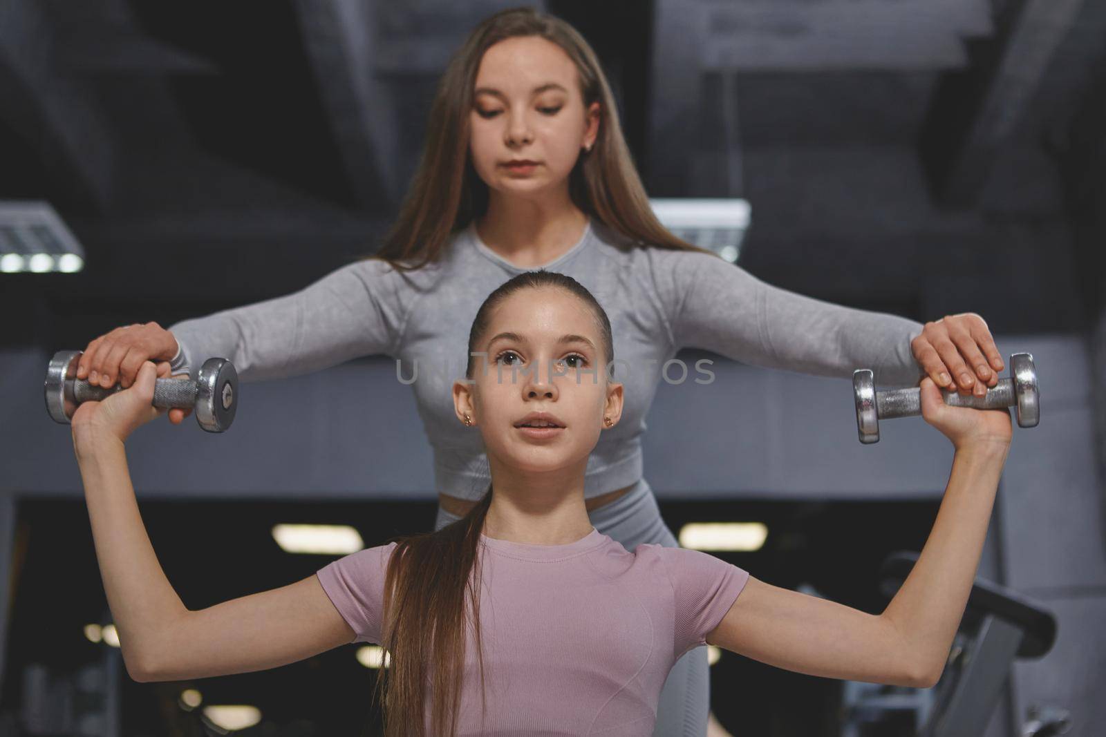 Teenage girl working out with dumbbells with personal trainer at the gym