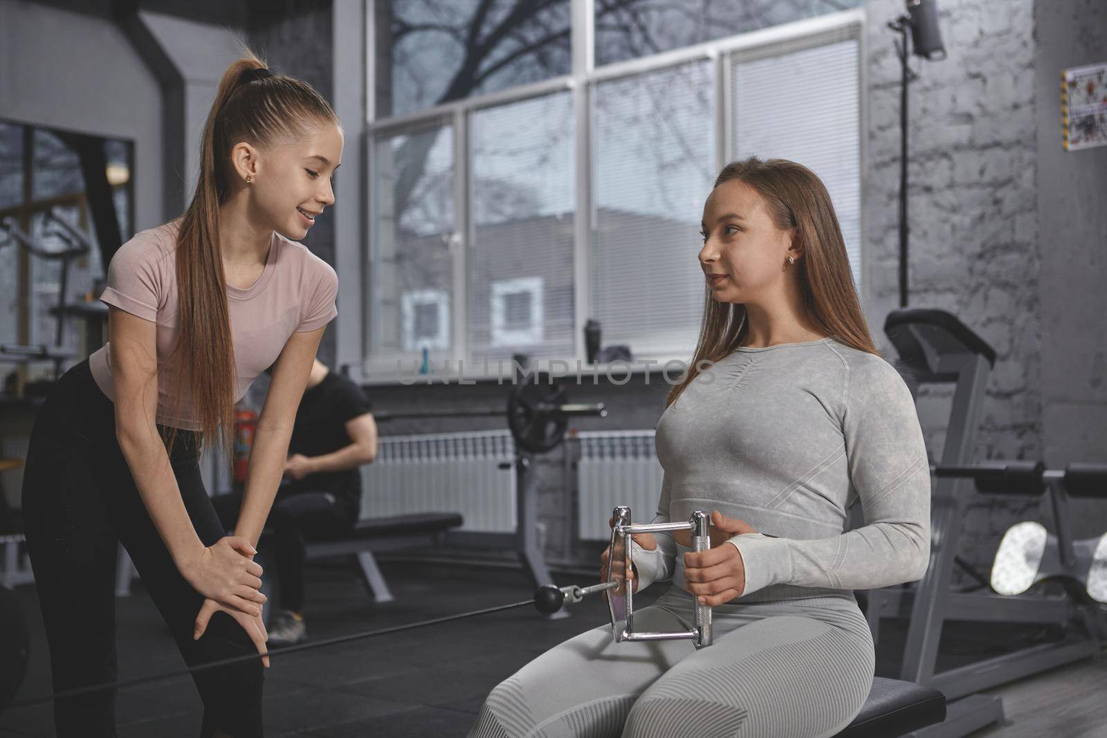 Teen girl watching her personal trainer explaing rowing machine exercise