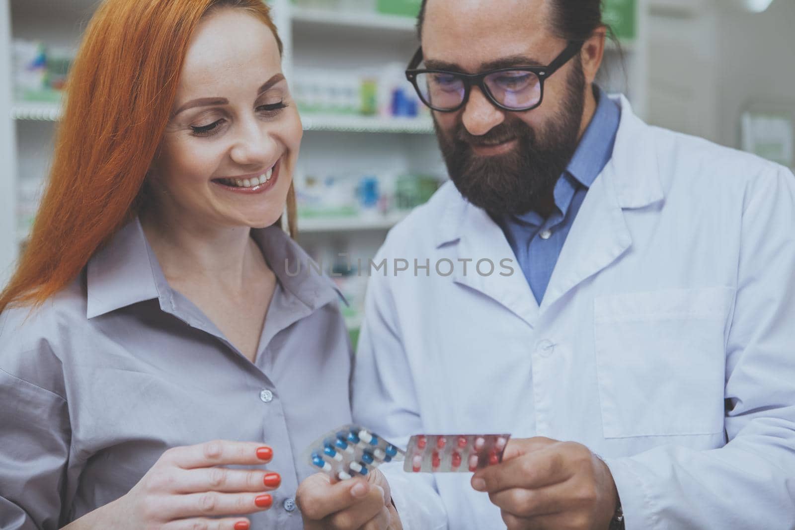 Cropped shot of a bearded pharmacist helping his cheerful female customer choosing medication to buy. Charming woman smiling, buying medicine from experienced chemist at the pharmacy