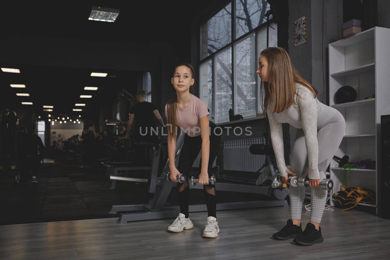 Full length shot of a teen girl and her personal trainer doing dumbbells deadlift exercise at the gym, copy space