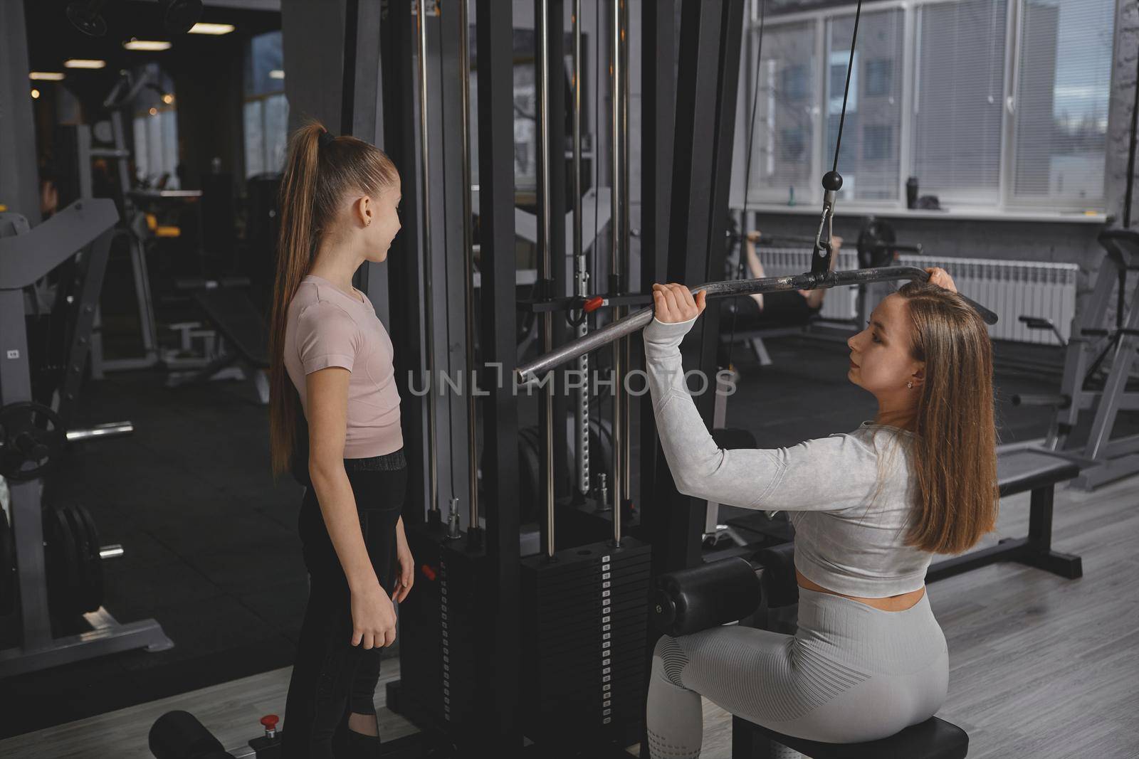 Personal trainer teaching teen girl working out on lat pull down gym machine