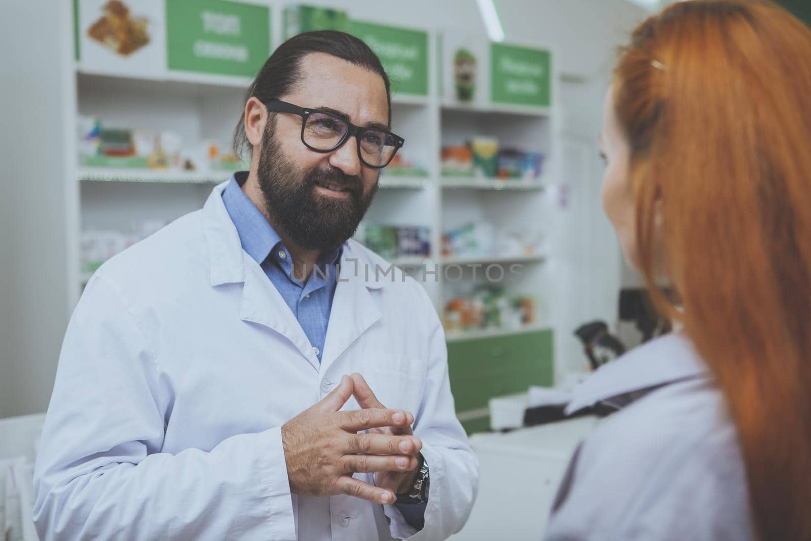 Cheerful male pharmacist helping female customer buying medications at the drugstore. Bearded chemist working at pharmacy, giving medical advise to the patient. Communication, medical care concept