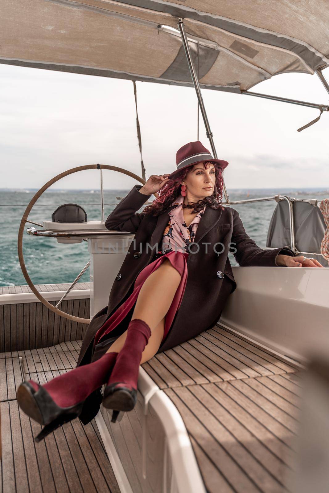 Attractive middle-aged woman at the helm of a yacht on a summer day. Luxury summer adventure, outdoor activities. by Matiunina