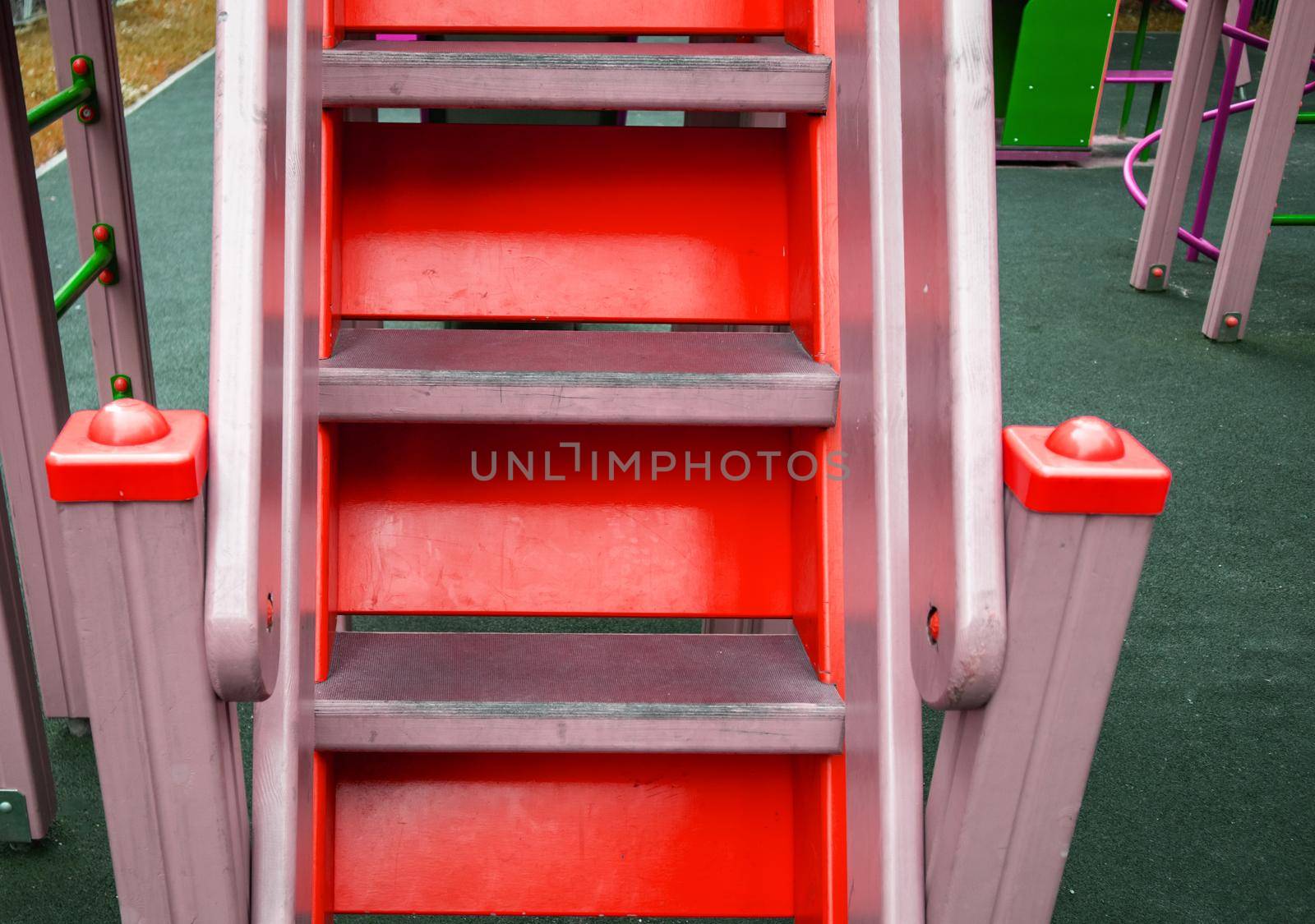 Close-up of wooden steps on an empty red staircase in an outdoor playground, a safe play area for children.