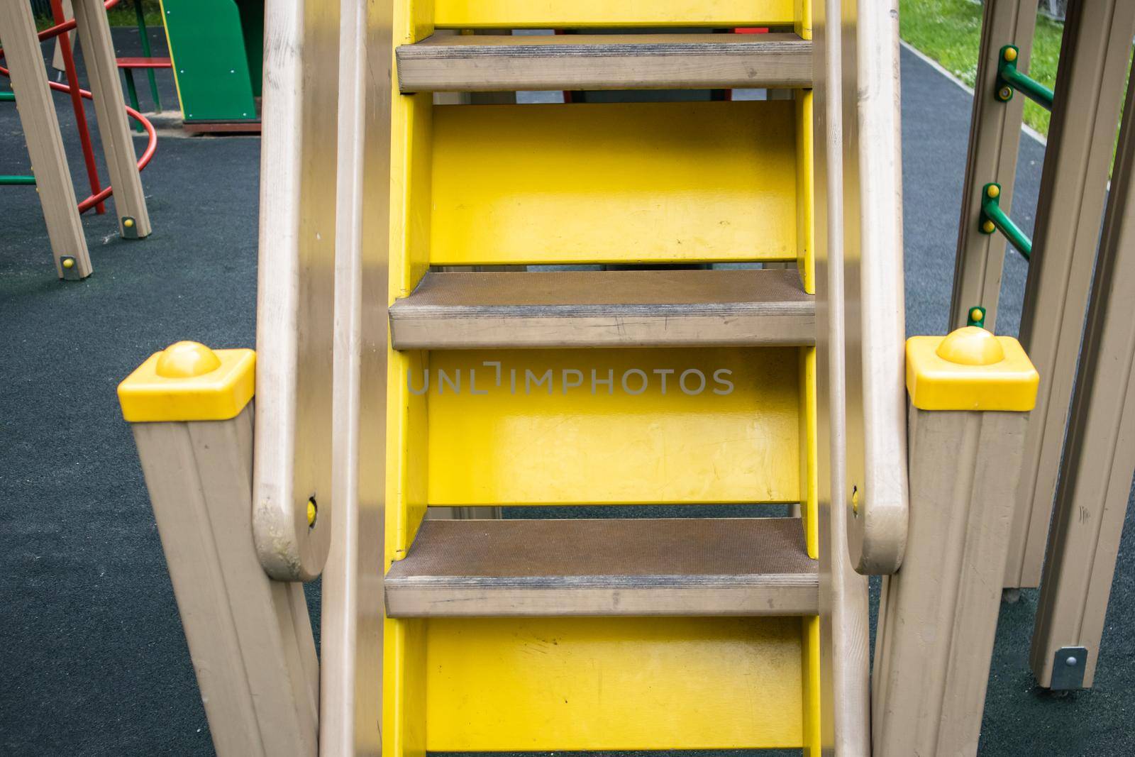 Close-up of wooden steps on an empty yellow staircase on an outdoor playground, a safe play area for children.