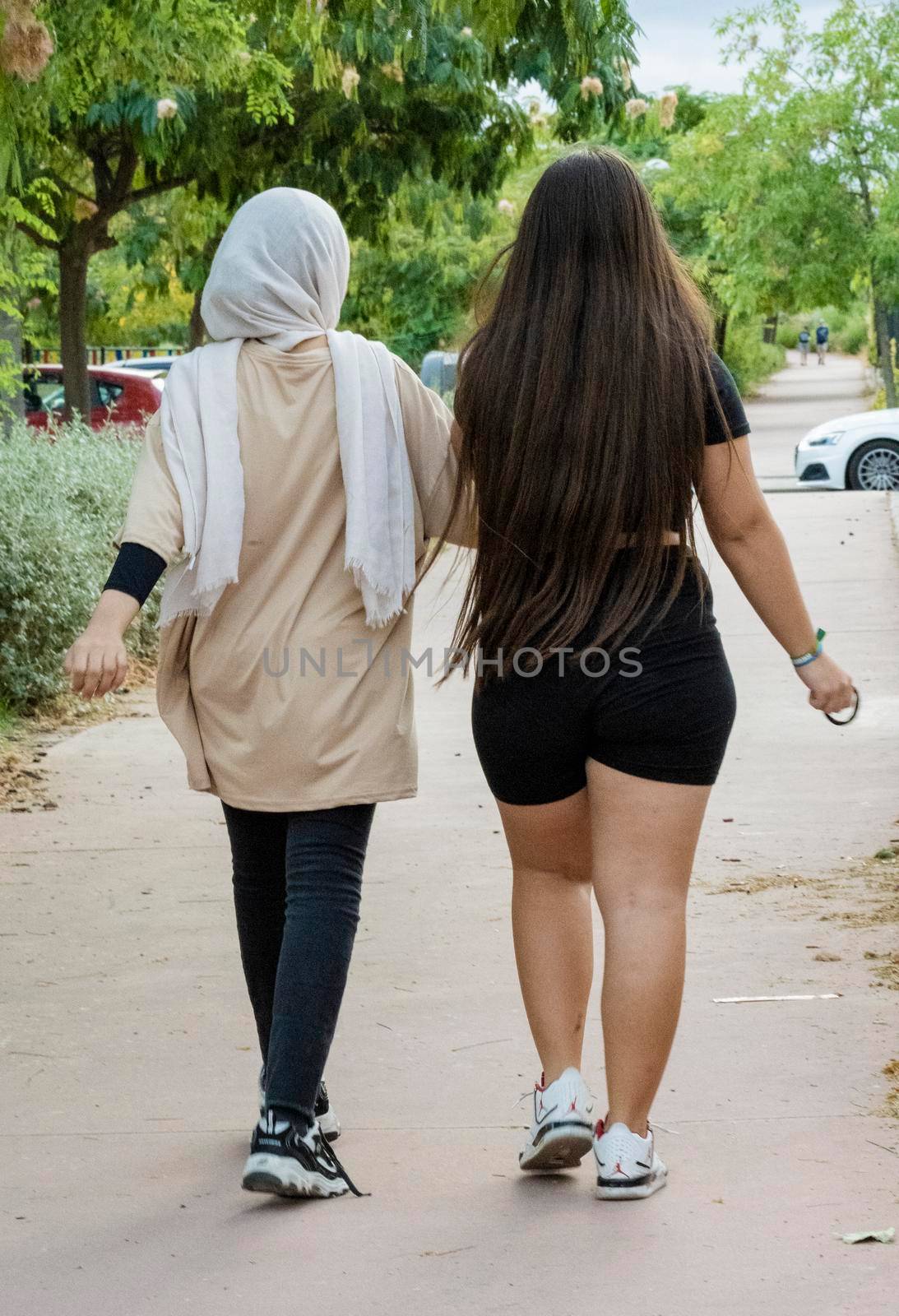 Arabic and european teen girls walking and enjoying time together in a park. Multicultural and multiethnic concept.