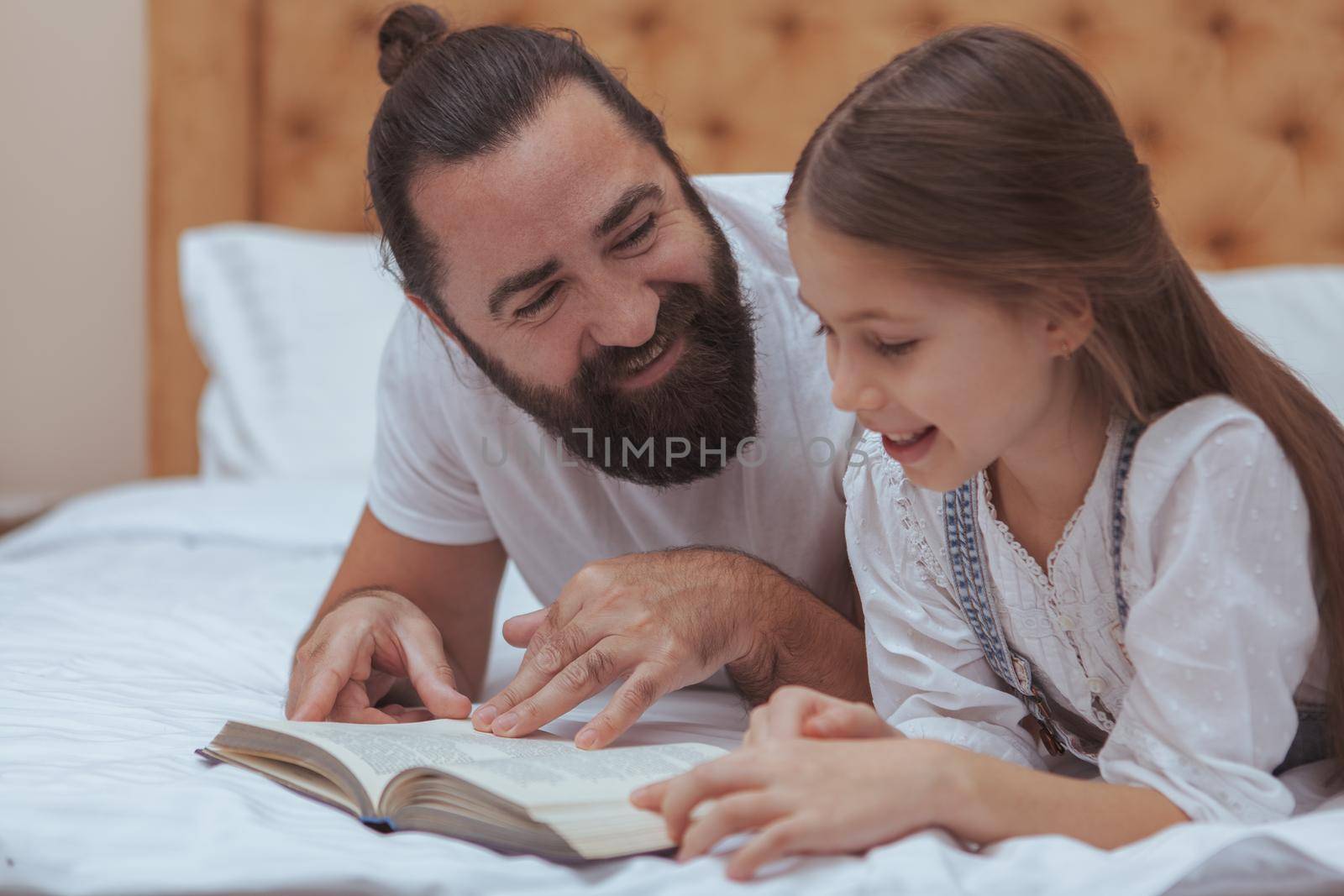 Beautiful little girl enjoying reading a book with her father. Single dad studying with his little daughter. Handsome bearded man reading books to his child