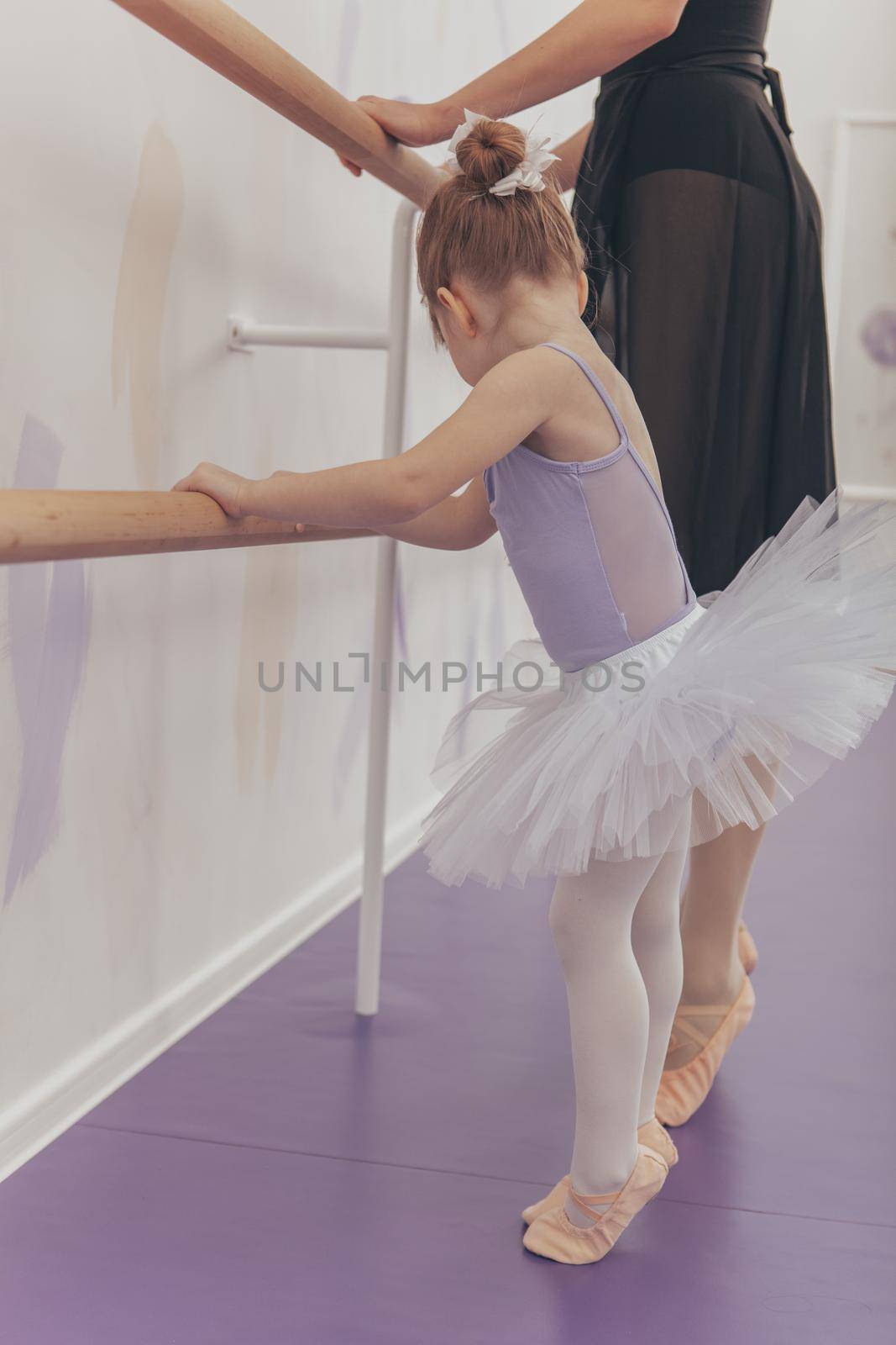 Vertical shot of an adorable little ballerina exercising at ballet school with her teacher. Cute little girl in tutu and leotard learning dancing ballet from professional ballerina