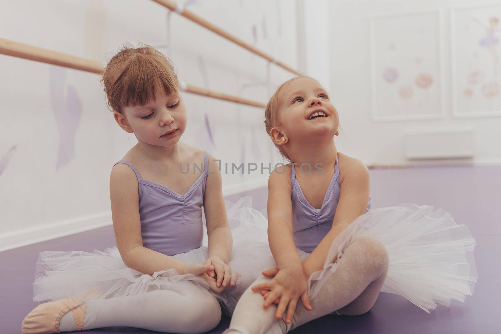 Cheerful little ballerinas having fun together at dance school. Adorable little girls sitting together on the floor, relaxing after ballet lesson. Adorable little friends at ballet studio