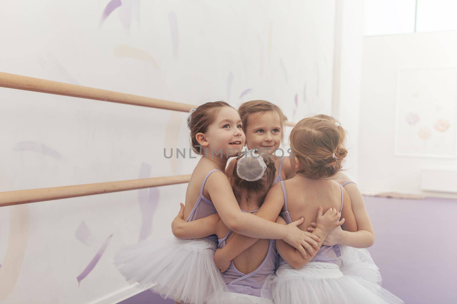 Adorable litlle ballerinas having fun at dance studio, smiling and hugging together. Group of cute little girls in tutu skirts celebrating, embracing each other. Unity, friendship, childhood concept