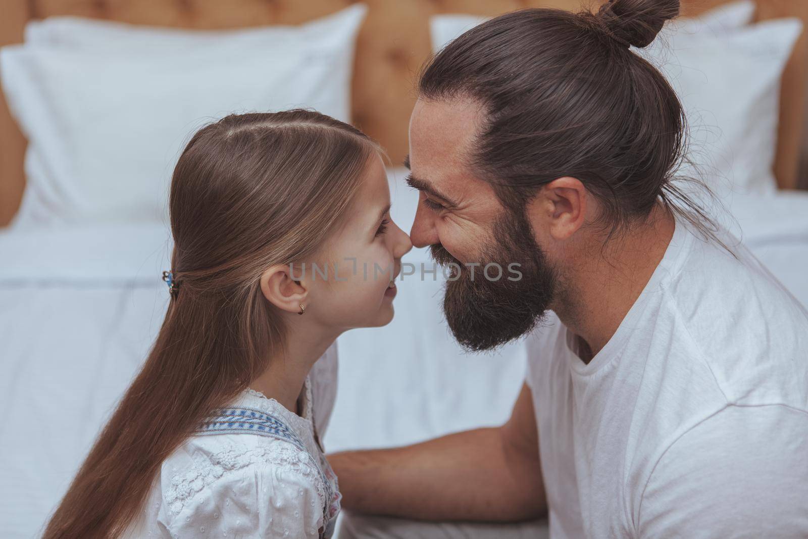 Close up of happy father and daughter touching with noses, enjoying weekend at home together. Adorable little girl rubbing noses with her dad