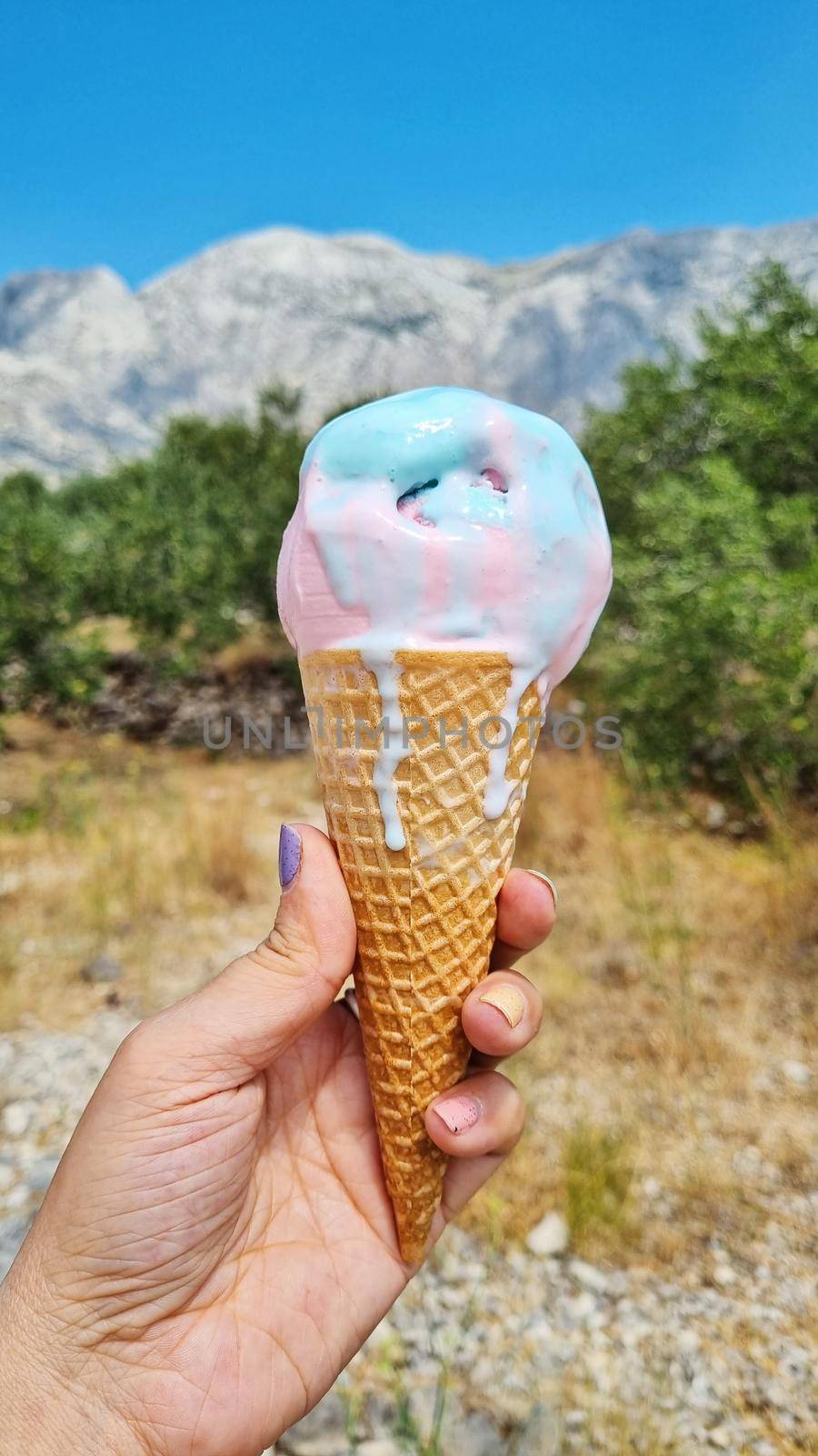 Melting gelato ice cream cone held up to the hot summer day.