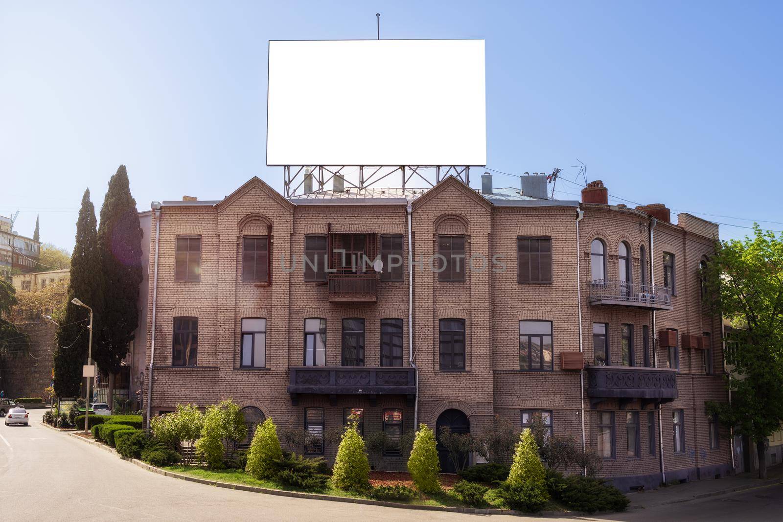 Mockup, template. Big, white, blank banner for your design and space for text. City landscape on a summer day. Large historical building and road in front of it, green trees and bushes