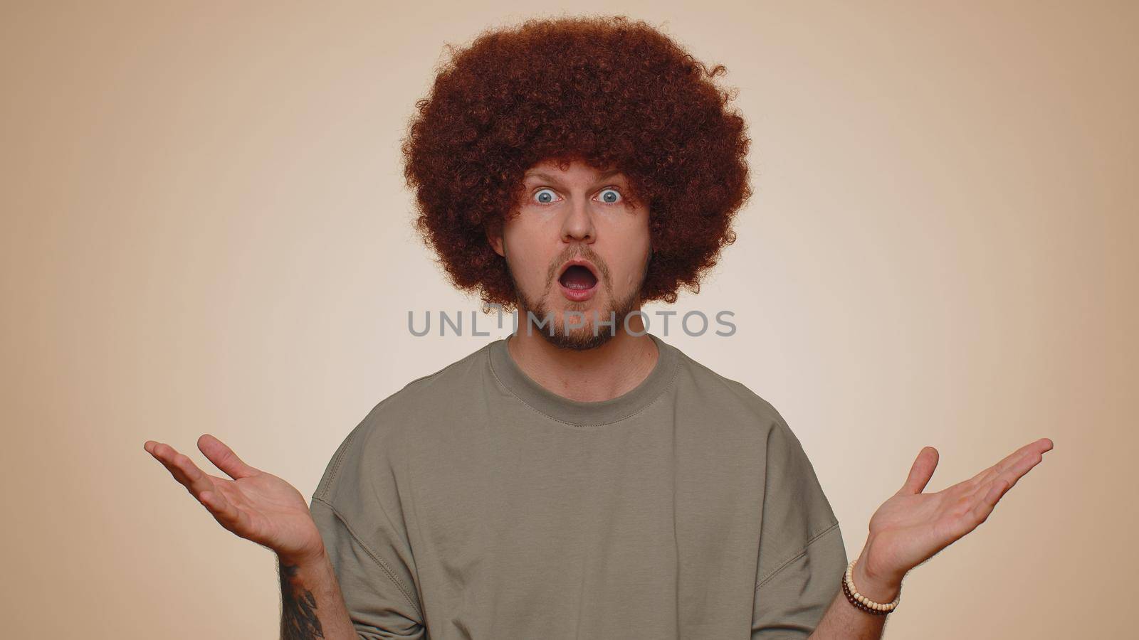 Oh my God, Wow. Excited amazed winner man raising hands in surprise looking at camera with big eyes, shocked by sudden victory. Sincere young adult guy boy isolated alone on beige studio background