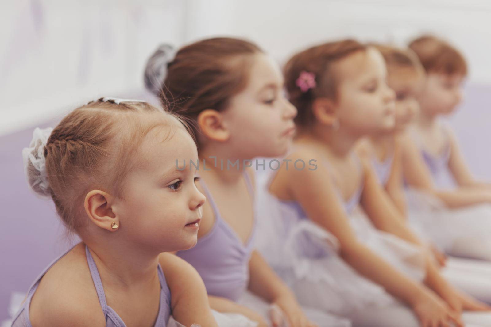 Close up of a beautiful little ballerina girl sitting with her classmates at ballet school. Group of cute little girls at dance studio. Children, kids, childhood concept