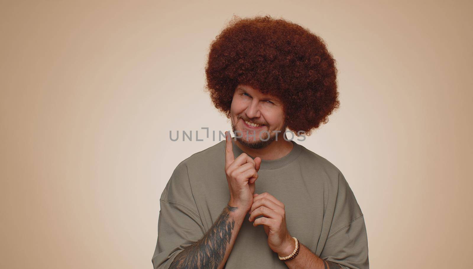 Sneaky cunning man with tricky face gesticulating and scheming evil plan, thinking over devious villain idea, cunning cheats, jokes and pranks. Young guy on beige studio wall background alone indoors