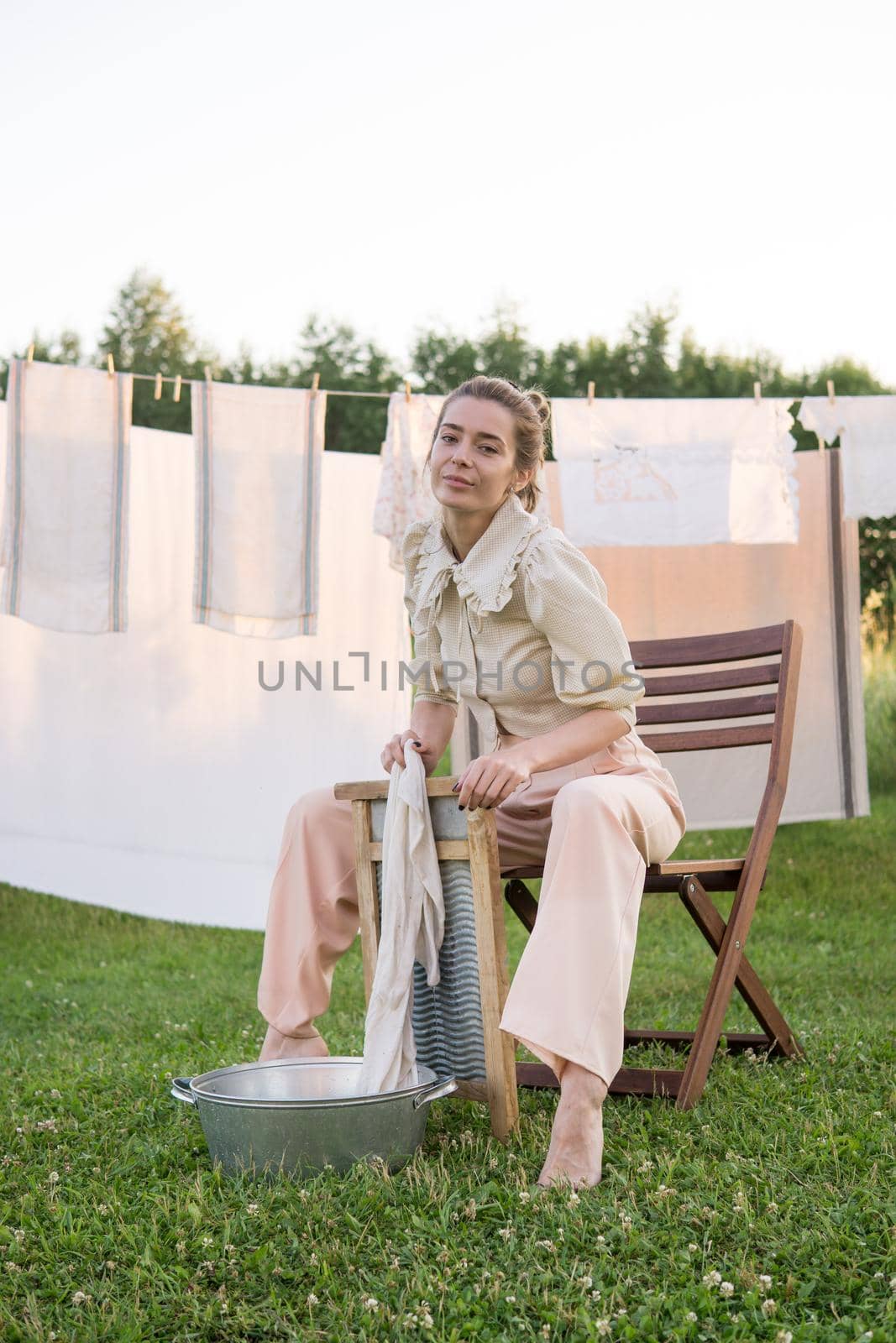 Laundry day. A woman hangs linen and towels on a tree in the courtyard of a village house. Summer cottage concept.