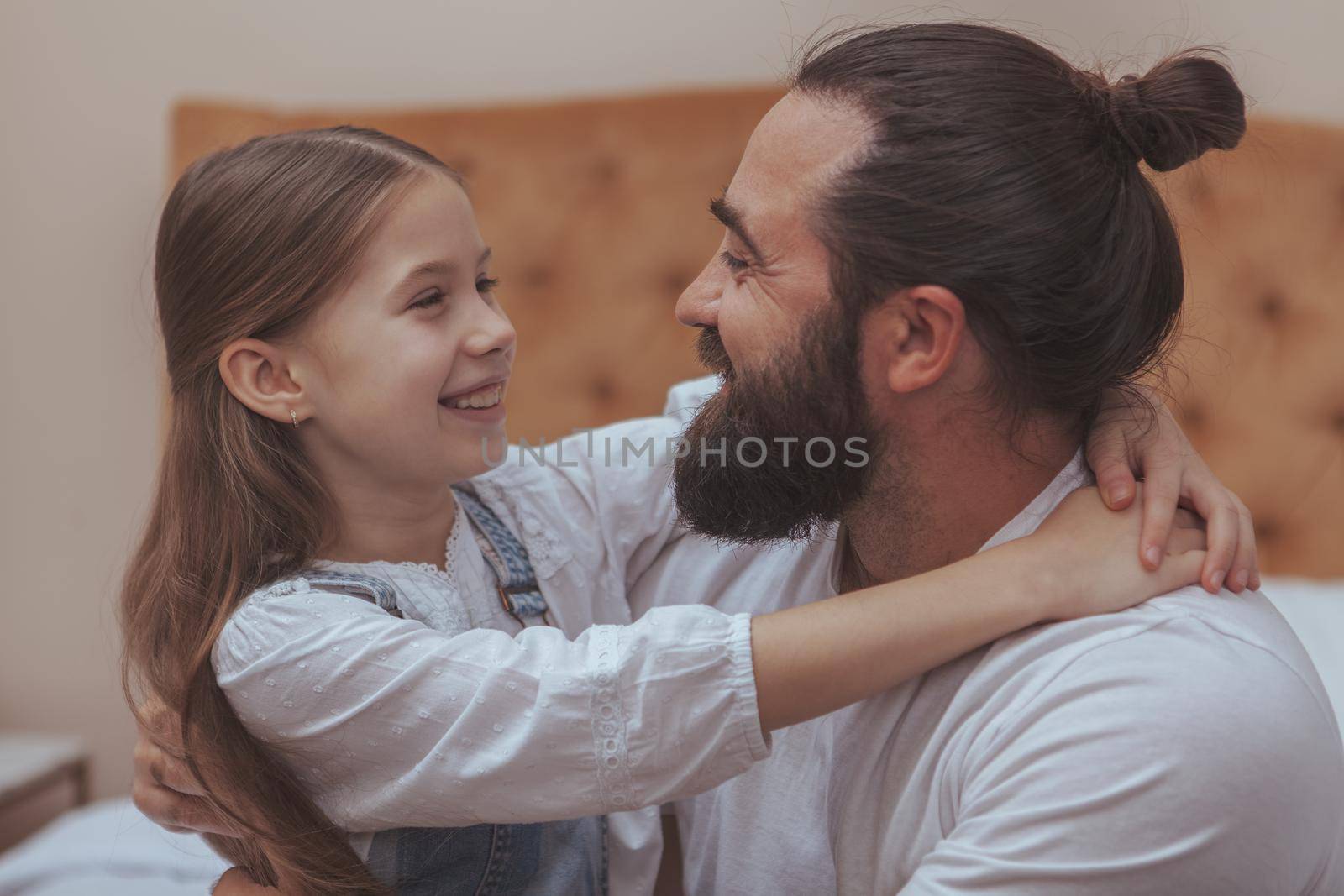 Happy father and daughter hugging, smiling at each other, having fun at home. Handsome bearded mature man embracing his adorable little daughter