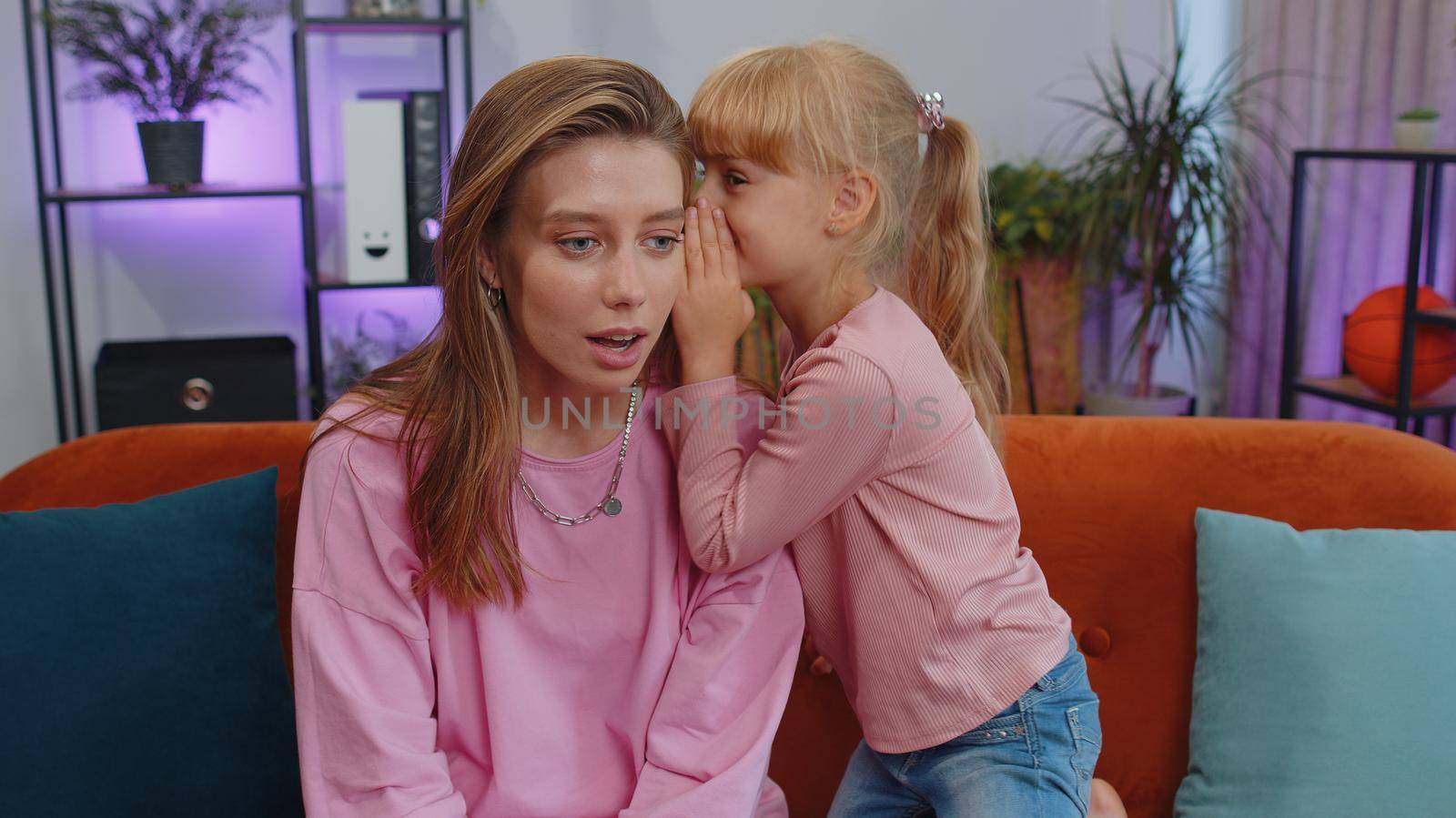 Little daughter child kid whispering in cheerful loving mom ear, telling secret with joyful amazed mom. Girl telling funny story, joke to young mother or nanny, enjoying friendship, trust, motherhood