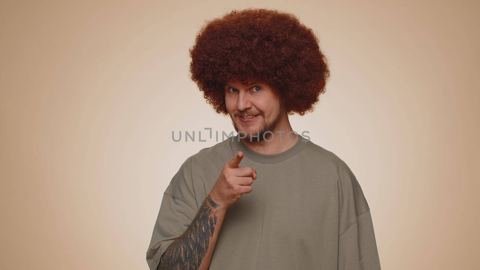 Hey you. Man 30s in t-shirt smiling excitedly and pointing to camera, choosing lucky lottery winner, indicating to awesome you. Young adult guy boy isolated alone on beige studio wall background