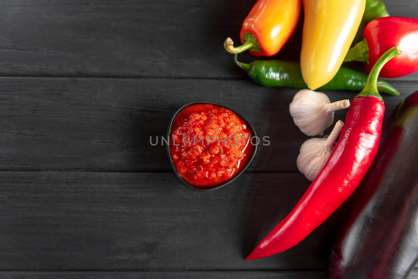 Ajvar in a black bowl with the ingredients red pepper chili peppers garlic on a wooden background. A classic Balkan dish