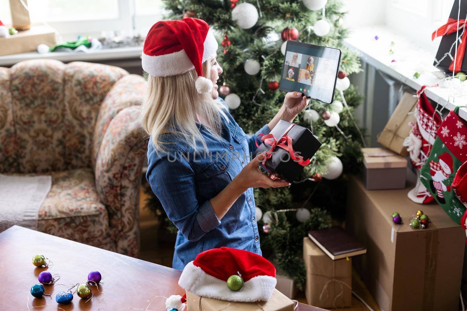 A middle-aged blonde woman uses a tablet for a video call while sitting in an armchair by Andelov13