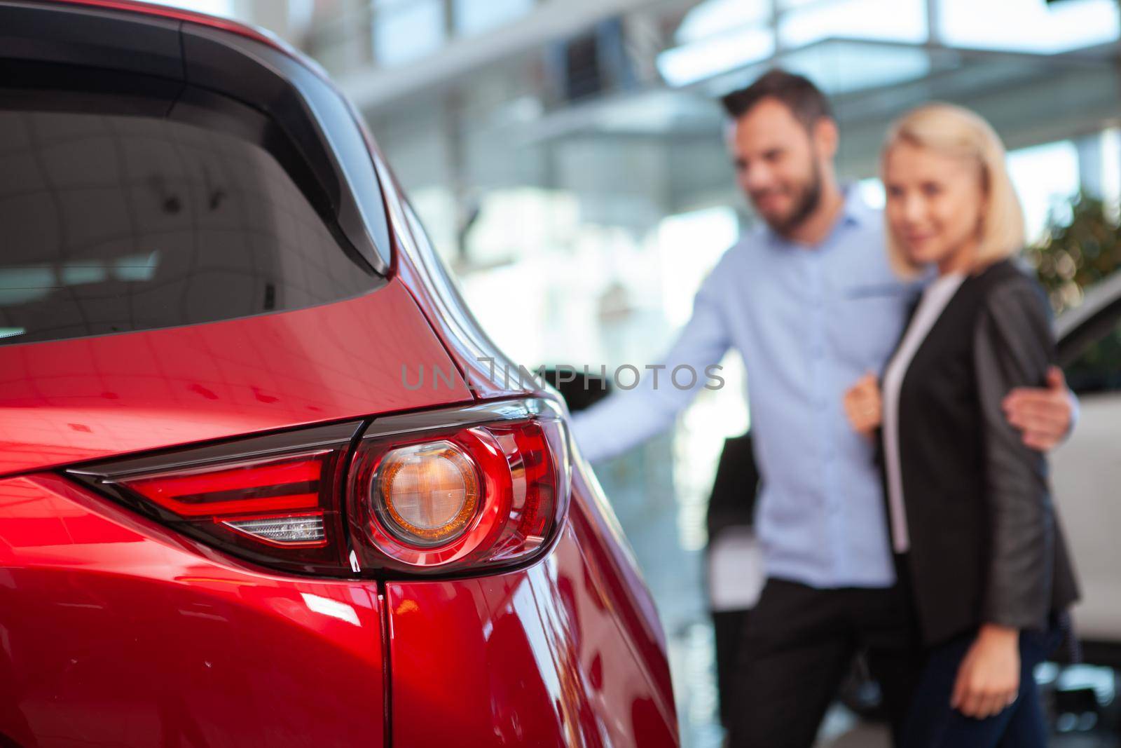 Selective focus on car light, couple examining automobile for sale on background. Young family buying new auto together at the dealership