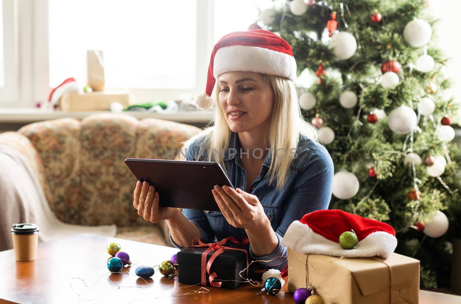 Christmas online holiday. Happy woman having video call with their family or friends. Young woman uses a digital tablet near decorated festive tree at home. Virtual meeting.