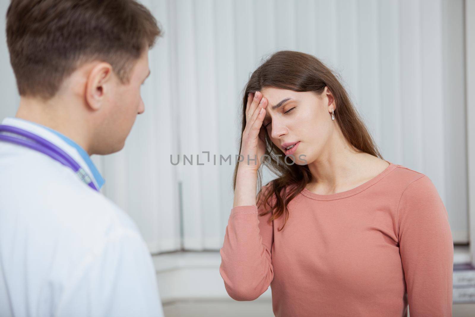 Young woman with fever or headache talking to the doctor. Sick female patient with migraine on medical appointment