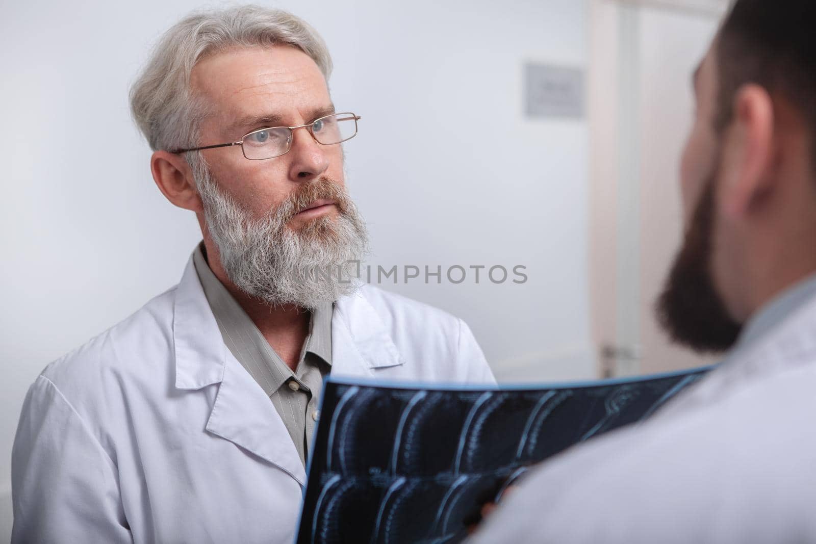 Senior medical worker talking to his colleague, holding MRI scan. Elderly male doctor discussing MRI of a patient with a co-worker