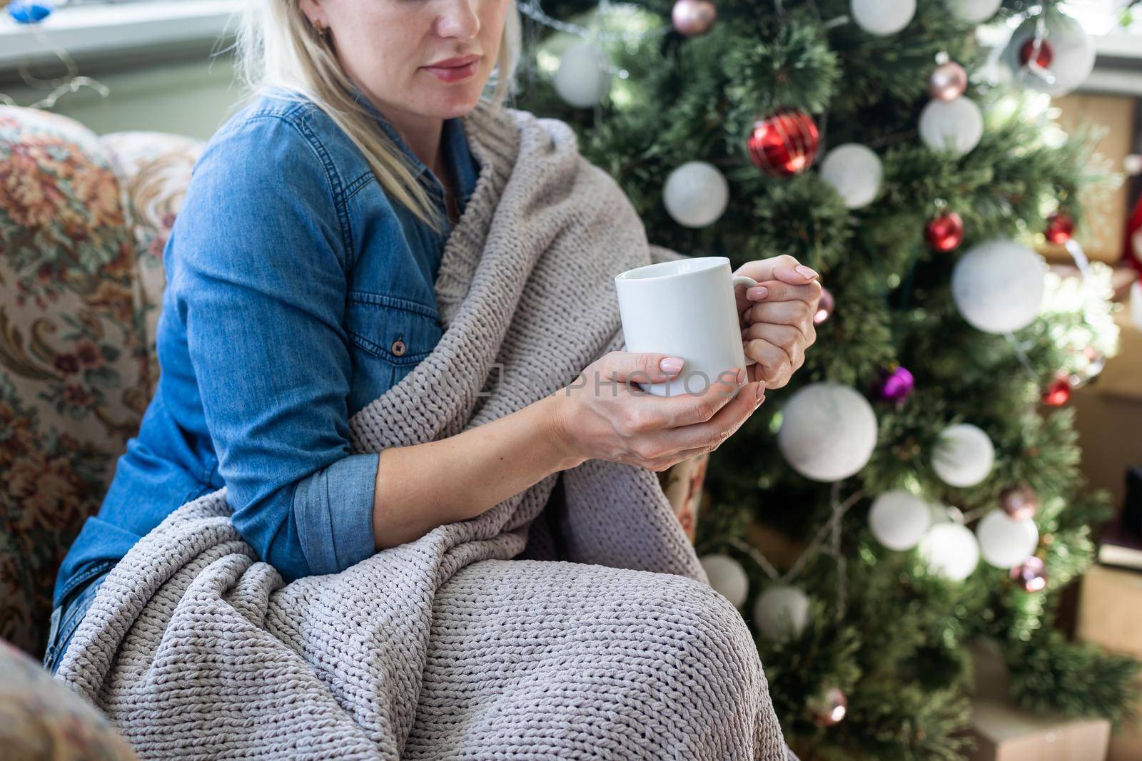 Young hispanic girl drinking coffee sitting on the sofa by christmas tree at home