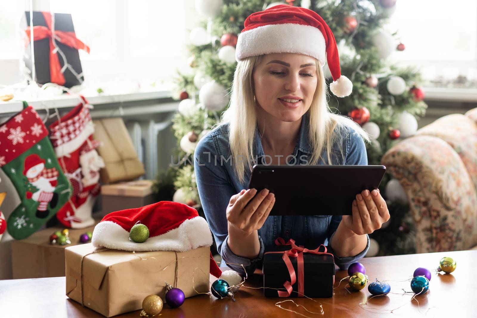 Woman with santa hat using video call conference on tablet, decorations and lights at home. Caucasian adult for christmas eve party by Andelov13