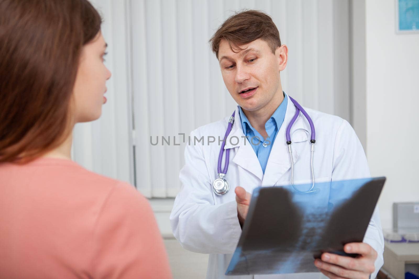 Experienced male doctor explaining x-ray scanning results to his female patient, working at his office