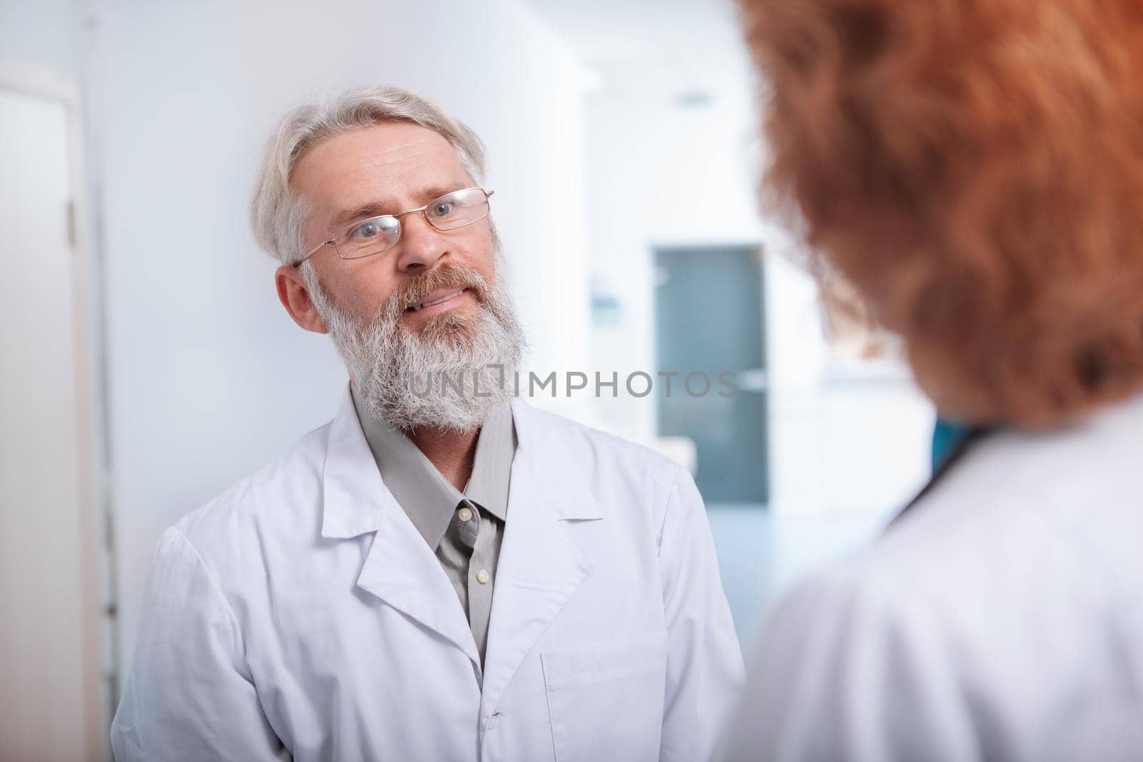 Happy senior male doctor smiling, talking to a female colleague at clinic hall