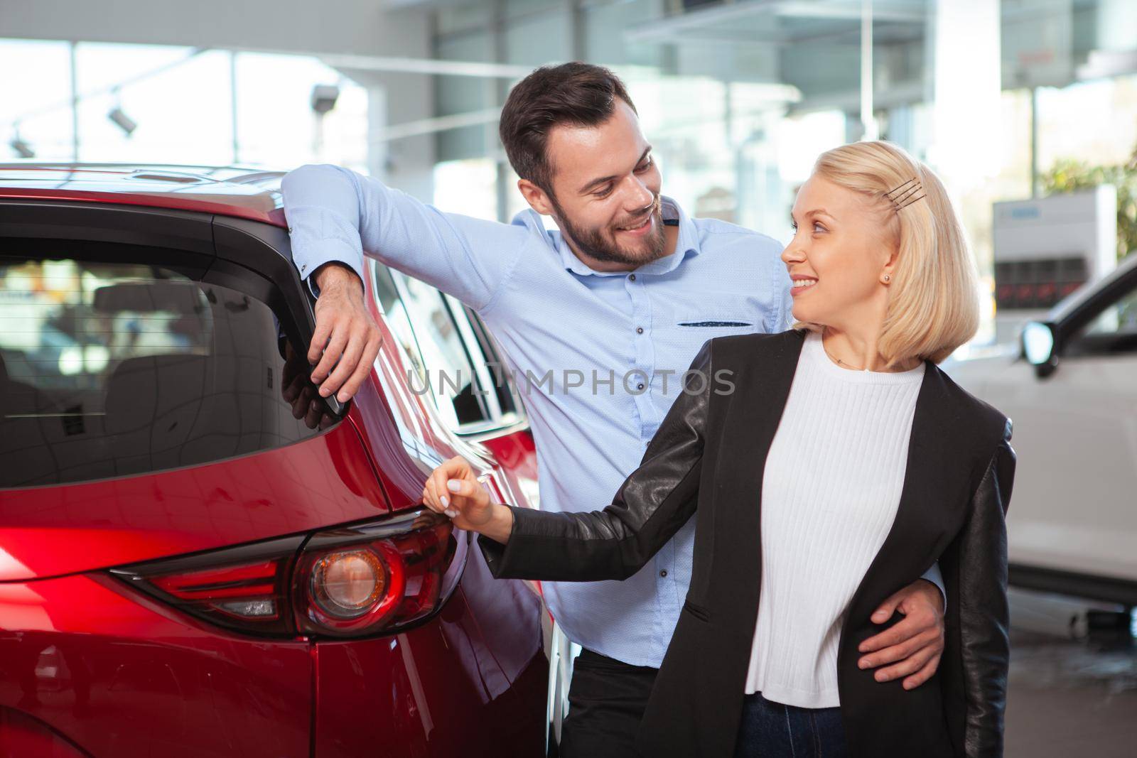 Happy couple hugging, smiling at each other at the dealership. Happy husband and wife buying new automobile