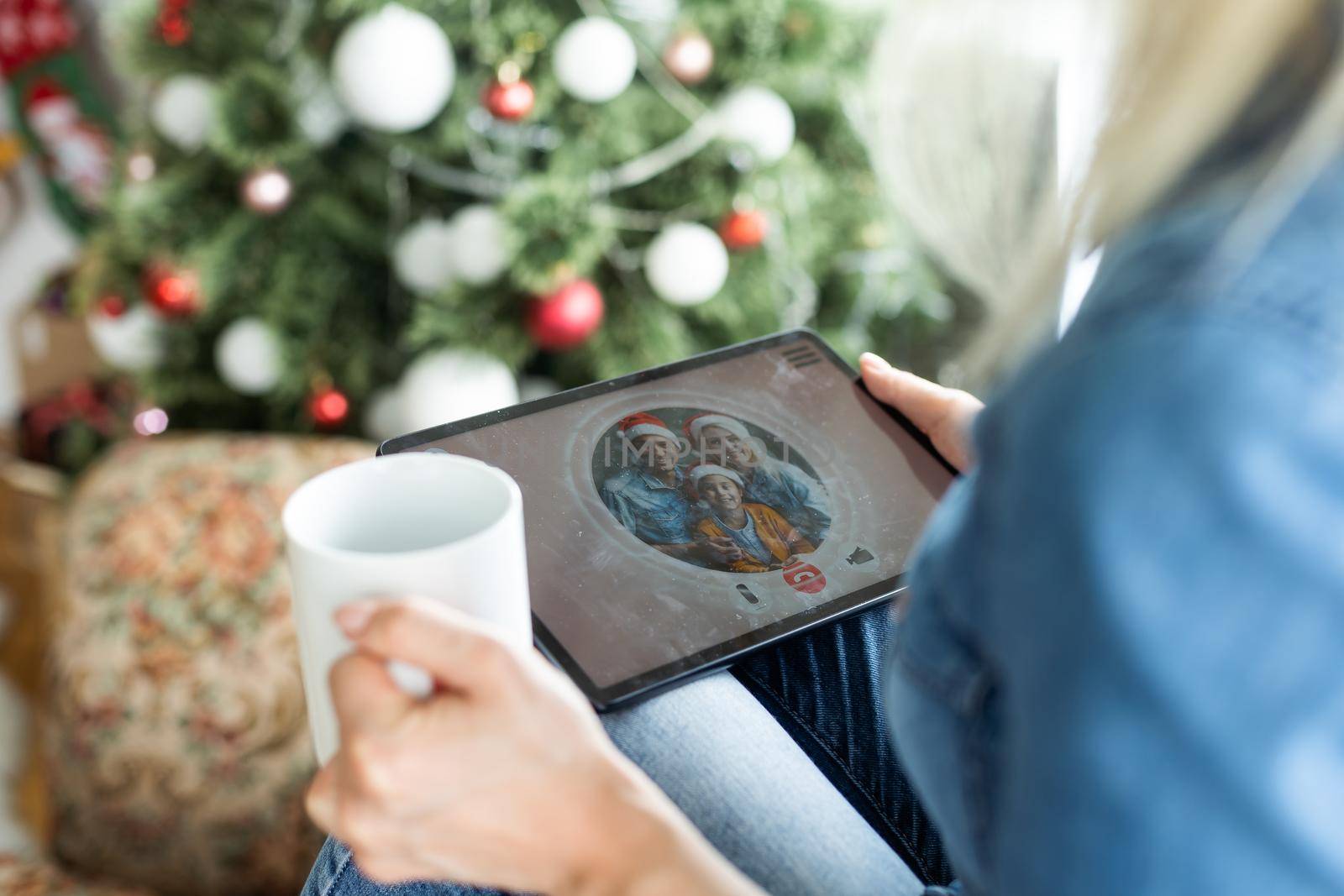 Christmas online holiday. Happy woman having video call with their family or friends. Young woman uses a digital tablet near decorated festive tree at home. Virtual meeting.