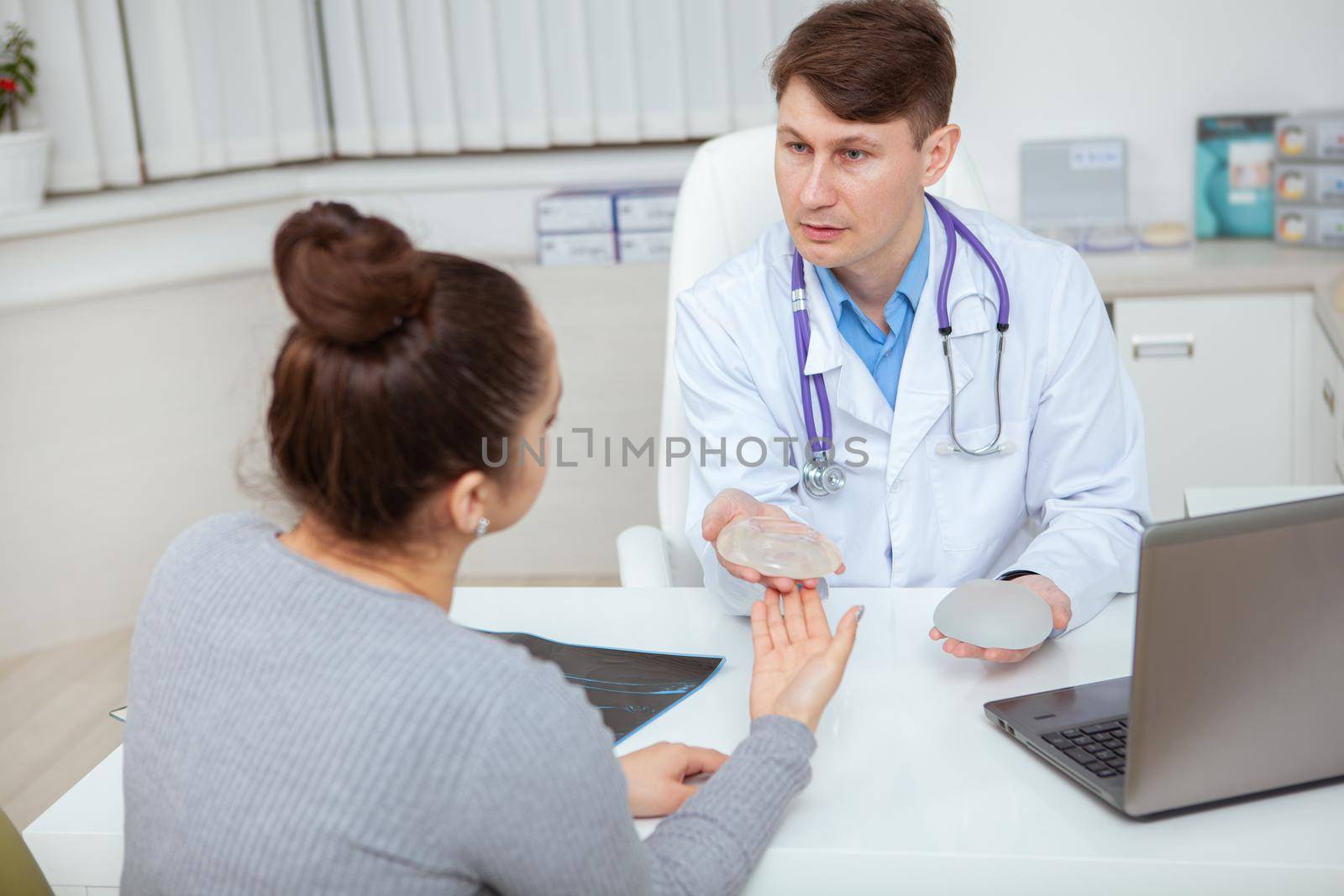 Professional plastic surgeon showing silicone breast implants to his female patient. Unrecognizable woman preparing for breast augmentation